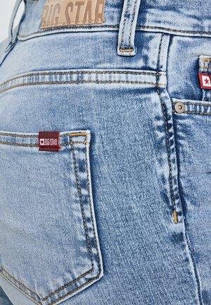 Hele sinised teksapüksid, millel on Big Star brändi nahast silt ja tagataskutel punased kangast sildid, näidates õmblusi ja metallist ninnikuid.