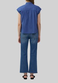 Blauw knoop-overhemd met korte mouwen en een geplooide achterkant, gecombineerd met high-waisted flared denim jeans en zwarte sandalen.