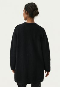 Svart stickad cardigan med en lös passform, strukturerat mönster, långa ärmar och rak kant, designad för bekväm lagerpåläggning.