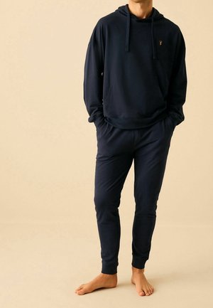 Námořnický modrý bavlněný hoodie s klokaní kapsou a nastavitelným šňůrkovým stahováním, spárovaný s odpovídajícími joggerami s elastickým pasem a manžetami.