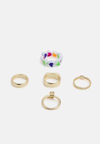 Quatro anéis: três bandas de metal dourado em várias larguras e acabamentos, mais um anel macio com padrão de corações coloridos.