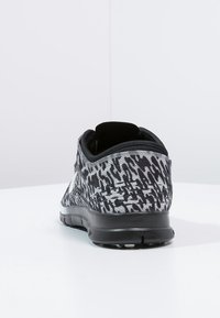 Sort og grå atletiksko med en struktureret stof-overdel, afrundet hæl og mønster i kontrast. Gummiydersål med slidbanedetaljer.