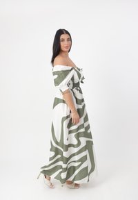 Abito lungo con design off-shoulder in bianco con motivi astratti verdi. Tessuto morbido, vita elastica e maniche arrotolate.