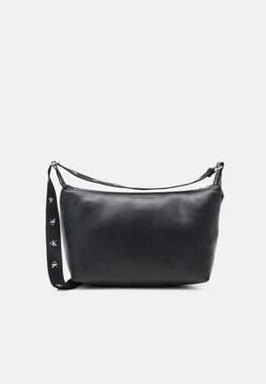 Schwarze Lederschultertasche mit verstellbarem Riemen, der weiße "ck"-Logos zeigt, und einem dezenten, geprägten Markennamen in der vorderen Mitte.