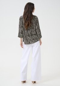 Black and white patterned blouse with three-quarter sleeves, paired with white wide-leg trousers and beige heels. Smooth texture and relaxed fit.