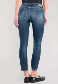 Jeans ajustados de mezclilla azul oscuro con una textura suave, cinco bolsillos y una pequeña etiqueta de marca en la parte posterior de la cintura.