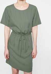 Robe verte à manches courtes avec un col rond et une taille cintrée. Fabriquée dans un tissu lisse, elle dispose d'un cordon de serrage pour un ajustement personnalisé.