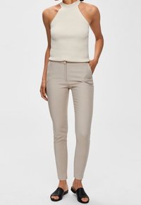 Vitt ribbat halter-top som kombineras med beige slim-fit byxor med sidorfickor. Modellen bär svarta slip-on sandaler.