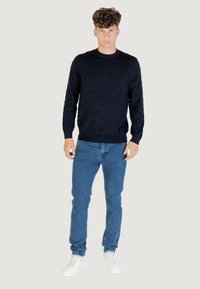 Marineblaues Strickpullover mit Wellenmuster, langen Ärmeln und Rundhalsausschnitt, kombiniert mit hellblauen Jeans und weißen Sneakers.