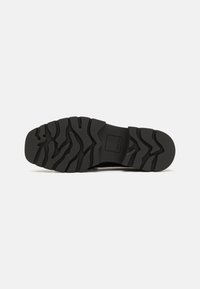 Black rubber shoe sole featuring a textured tread pattern with grooves and raised sections for traction and stability.