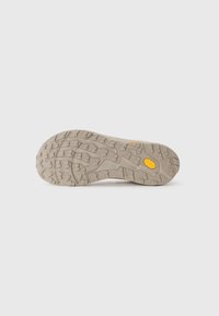 Semelle de chaussure de sport beige avec des motifs de trame profonds et un logo Vibram jaune sur fond blanc lisse.