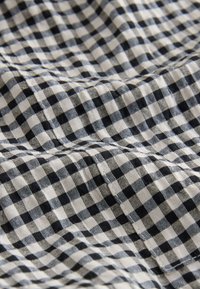 Katoenen stof met een zwart-wit ruitpatroon, bestaande uit kleine geruite vierkantjes. Gerimpelde textuur met zichtbare stikdetails.