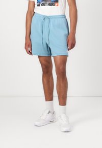 Ljusblå bomullsshorts med elastisk midja och dragsko. Har en liten vit logotyp. Bärs med vita sneakers och ankelsockar.