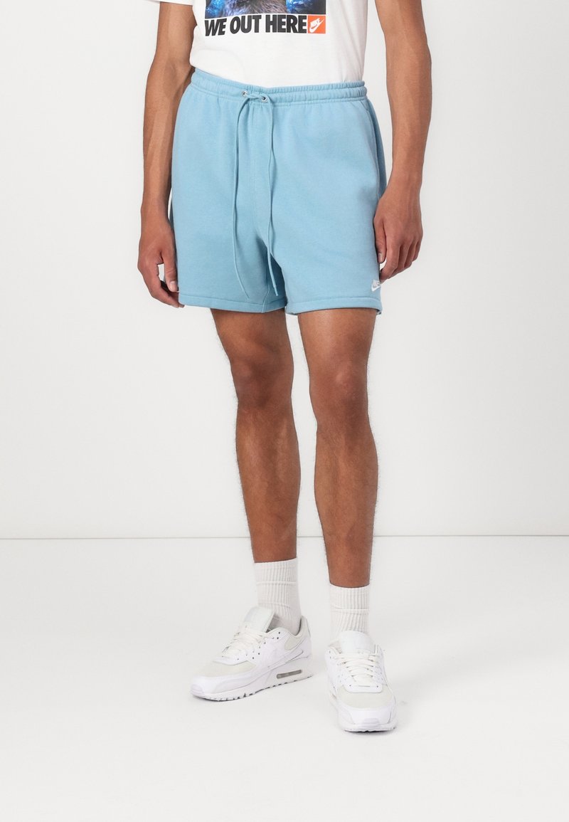 Ljusblå bomullsshorts med elastisk midja och dragsko. Har en liten vit logotyp. Bärs med vita sneakers och ankelsockar.