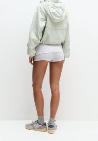 Lichtgroene windjack met capuchon, gecombineerd met grijze korte broek en grijze sokken. Schoeisel bestaat uit grijze en beige sneakers. Simpel, casual ontwerp.