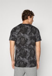 Zwarte t-shirt met een gestructureerd grijs patroon, korte mouwen en een ronde hals, weergegeven op een model van achteren.