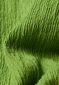 Grüner Stoff mit einer strukturierten, zerknitterten Oberfläche, die kleine, erhobene, horizontale Rillen und weiche Falten aufweist.