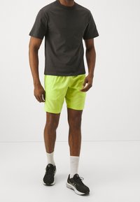 Černé tričko s krátkým rukávem, neonově žluté šortky, černé sportovní boty, bílé ponožky. Čistý design bez viditelných vzorů nebo log.