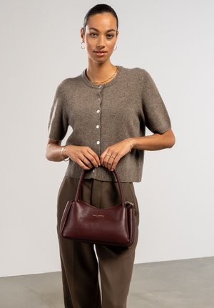 Gilet marron à manches courtes avec des boutons, associé à un pantalon taupe et un sac à main en cuir bourgogne à finition texturée et anses supérieures.