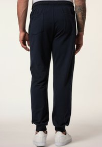 Marineblaue Jogginghose aus weichem Baumwollmix, mit einer lockeren Passform, elastischen Bündchen und zwei Gesäßtaschen. Kombiniert mit weißen Sneakers.