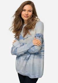 T-shirt à manches longues de couleur bleu clair avec un motif de montagne. Tissu doux, coupe décontractée, ourlet arrondi et manches allongées. Associé à un jean foncé.