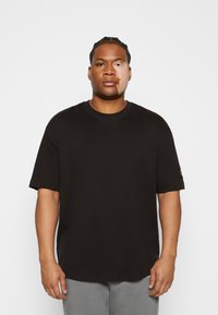 T-shirt in cotone nero con vestibilità rilassata, maniche corte e scollatura rotonda. Presenta un sottile dettaglio del logo su una manica.