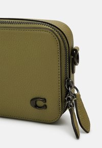 Portafoglio rettangolare in pelle verde oliva con finitura texturizzata, zip e hardware neri, dotato di un piccolo logo sulla parte anteriore e di una tracolla removibile.