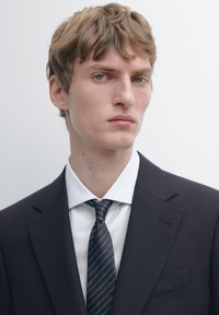 Ciemny dopasowany garnitur z klapami z wycięciem, biała koszula w paski oraz ciemnoszary krawat w paski; gładka tekstura, minimalistyczny design, neutralne tło.