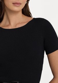 Černý žebrovaný top s kulatým výstřihem a krátkými rukávy, s hladkou texturou a těsným střihem.