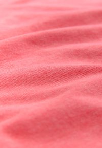 Mīksta koraļļu krāsas audums ar smalku adījuma tekstūru un vieglām viļņotām līnijām virsmas tekstūrā.