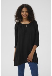 Tunique noire avec un col rond, détail froncé et ouverture en forme de clé avec bouton. Manches longues avec poignets, design fluide et texture douce.