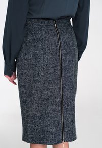 Teksturowana granatowa spódnica ołówkowa z widocznym suwakiem z tyłu i prostym sylwetką, zestawiona z dopasowaną, ciemną bluzką.