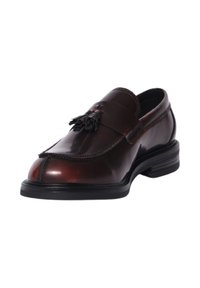 Mocassino in pelle marrone con finitura lucida, cinturino piegato e dettaglio decorativo con nappine. Presenta una punta arrotondata e un tacco basso nero.