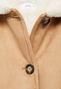 Giacca in faux suede tan con una morbida fodera bianca, dotata di chiusura a doppi bottoni e una superficie liscia.