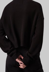 Černý crop svetr z žebrovaného úpletu, s širokými rukávy a volným střihem. Zadní část je hladká a končí nad pasem.