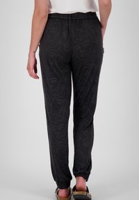 Svarta joggerbyxor med ett subtilt linjekonstmönster av ansikten. Har resårmidja och elastiska cuffs vid anklarna.