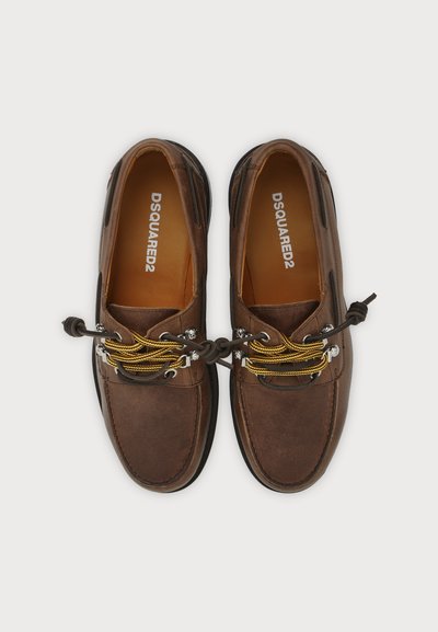 Paire de chaussures bateau en cuir marron avec des lacets jaunes et marron noués en nœud, marquage DSQUARED2 à l’intérieur de chaque chaussure, présentée sur fond blanc.