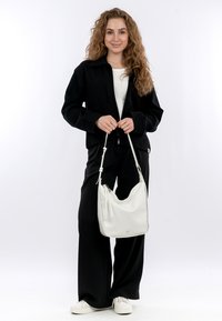 Jacket nera con zip sopra una maglietta bianca, abbinata a pantaloni neri a gamba larga e sneakers bianche. Una borsa a spalla in pelle bianca completa il look.