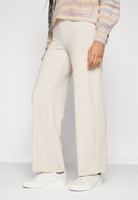 Pantaloni beige a gamba larga con coste, in tessuto knit leggero, design a vita alta, abbinati a sneakers bianche, dal fit casual.