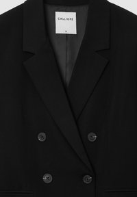 Blazer noir croisé avec larges revers et quatre boutons, doté d'une étiquette blanche à l'intérieur du col mentionnant "CALLIOPE" taille petite.