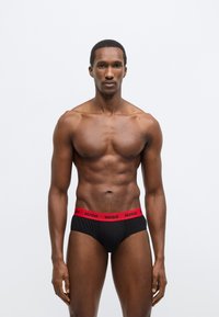 Čierne krátke spodné prádlo s červeným elastickým pásom s nápisom "HUGO". Hladká látka, priliehavý strih, minimalistický štýl.