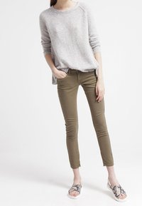 Ljusgrå stickad tröja, olivgröna åtsittande byxor och sandaler med ormiga mönster. Tröjan har en rundad halsringning och avslappnad passform.