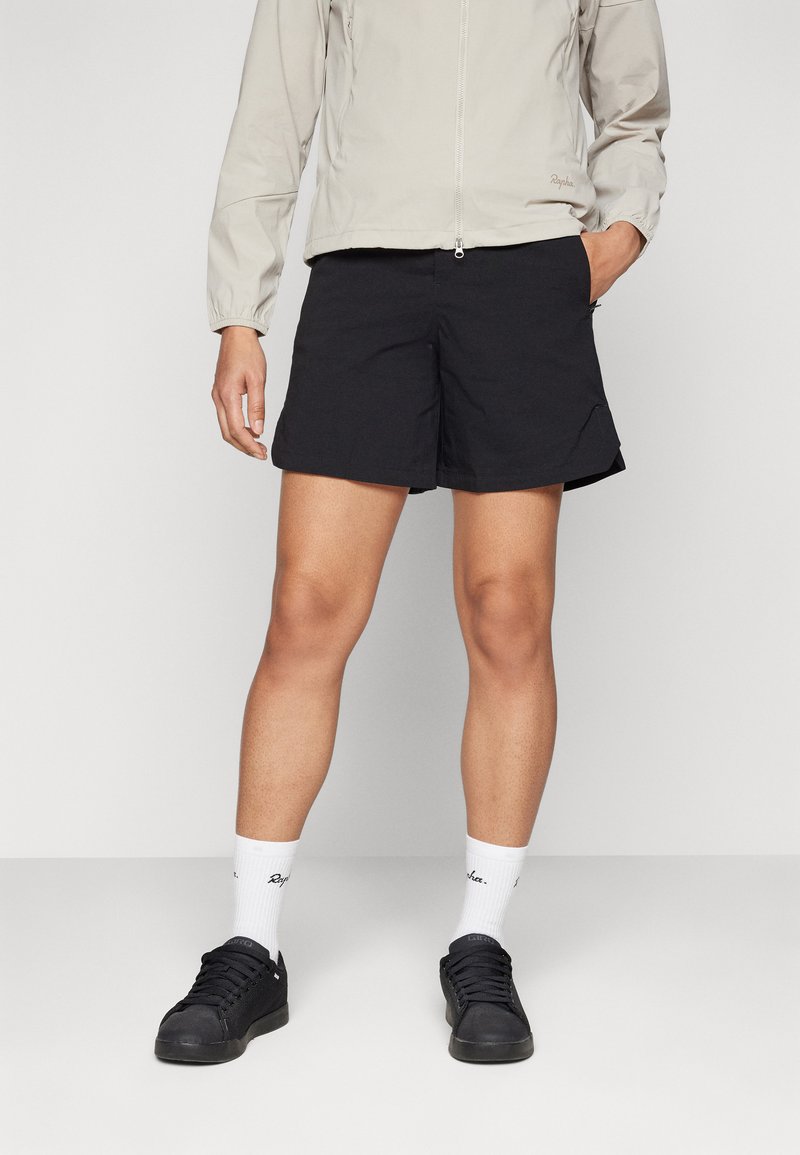 Shorts noirs en tissu léger, avec une coupe décontractée et des poches latérales. Associés à une veste zippée gris clair et des baskets noires.