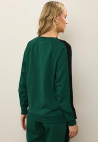 Felpa verde con pannelli laterali neri, polsini e orlo a coste. Tessuto liscio, scollatura rotonda e maniche raglan. Design minimalista.