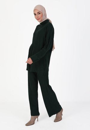 Dark green ribbed knit outfit featuring a high neck, loose fit top, and wide-leg pants. A light-colored hijab complements the look.