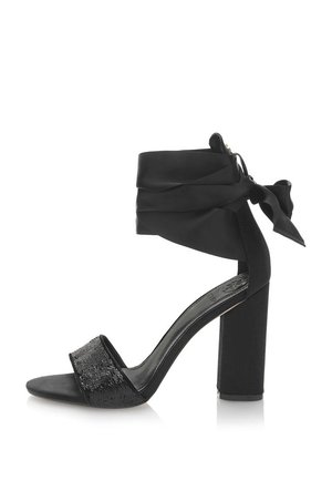 Sort højhælet sko med en blokhæl, stofankelomslag og en pailletdetalje. Har en glat overflade og åbent tådesign.