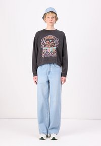 Black cropped sweatshirt with graphic design, light blue wide-leg jeans, and a light blue bucket hat. Sneakers with white and green accents.