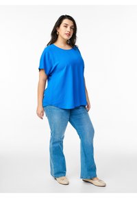 Blå kortærmet top med rund hals, parret med lyseblå flare jeans og beige flade sko, med en afslappet pasform og glat tekstur.