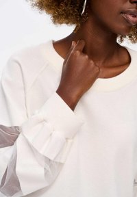 Witte sweatshirt met een ronde hals, getextureerde manchetten met doorschijnende ruffles en een ontspannen pasvorm. Geen zichtbare patronen of accenten.