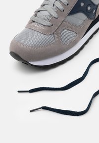 Sneaker in suede e rete grigia con accenti blu navy, caratterizzato da una parte superiore testurizzata, design con lacci e una suola in gomma nera. Include un laccio di scorta blu scuro.